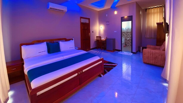 A modern hotel room with a large bed, a desk, and a seating area. - Gombe Park Hotel (Morogoro)