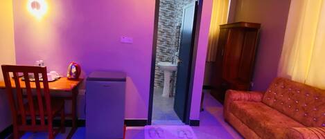 A compact living space with a dining area, a small refrigerator, a sofa, and a bathroom visible through a doorway.