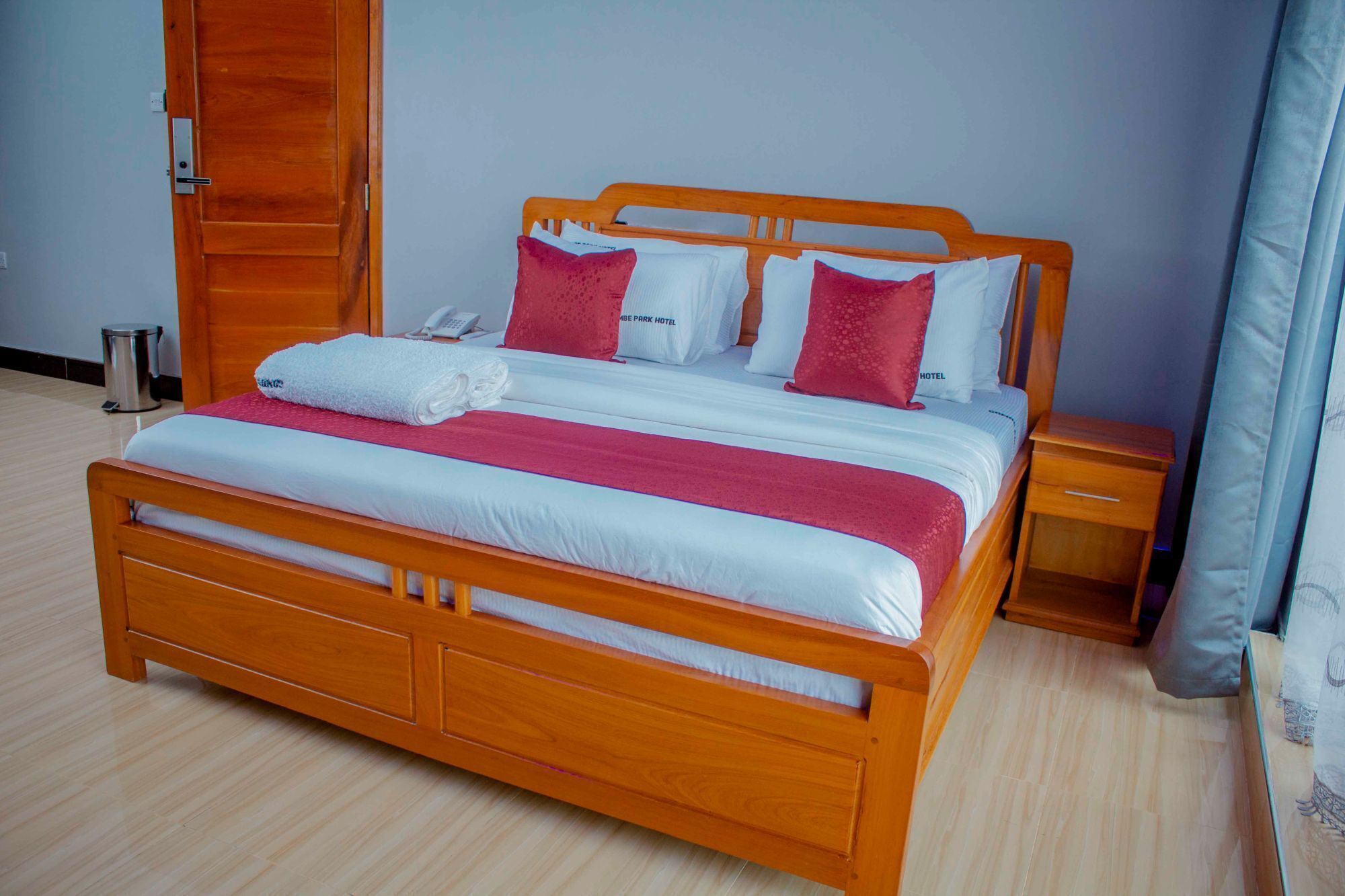 A wooden bed with white and red bedding, a bedside table, and a curtain.