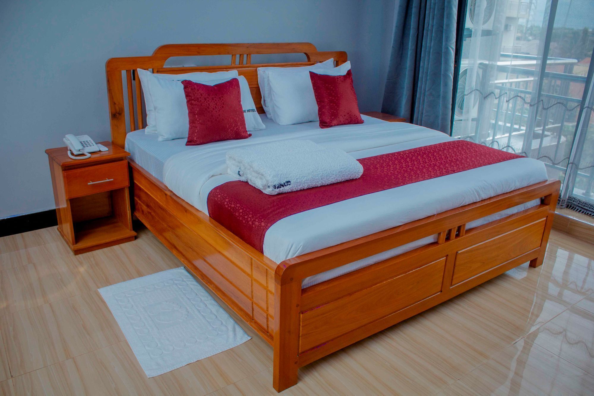 A wooden bed with a white and red bedspread, a white blanket, and a red pillow. There is a wooden nightstand with a white phone on it.