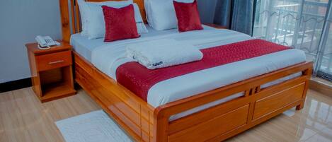 A wooden bed with a white and red bedspread, a white blanket, and a red pillow. There is a wooden nightstand with a white phone on it.
