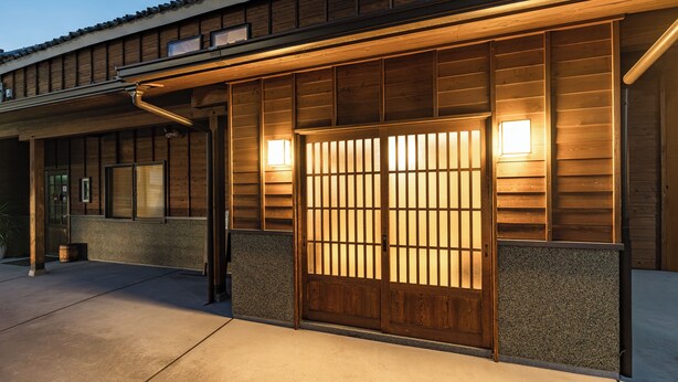 A traditional wooden building with a large wooden door and two wall-mounted lights. - Aburaya Bettei (Beppu)
