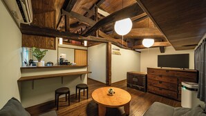 A cozy living room with a wooden ceiling, a round wooden table, a sofa, a TV, and a cabinet. - Aburaya Bettei (Beppu)