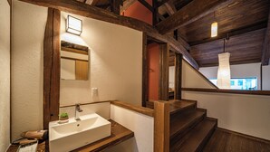 A bathroom with a wooden vanity, a white sink, a mirror, and a small potted plant. - Aburaya Bettei (Beppu)