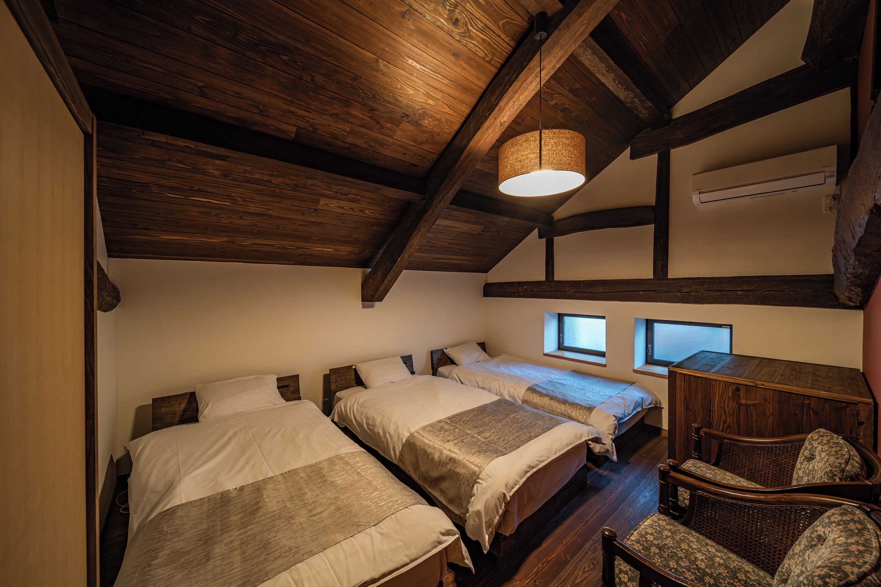 Un dormitorio con dos camas, vigas de madera, una lámpara colgante y una ventana.