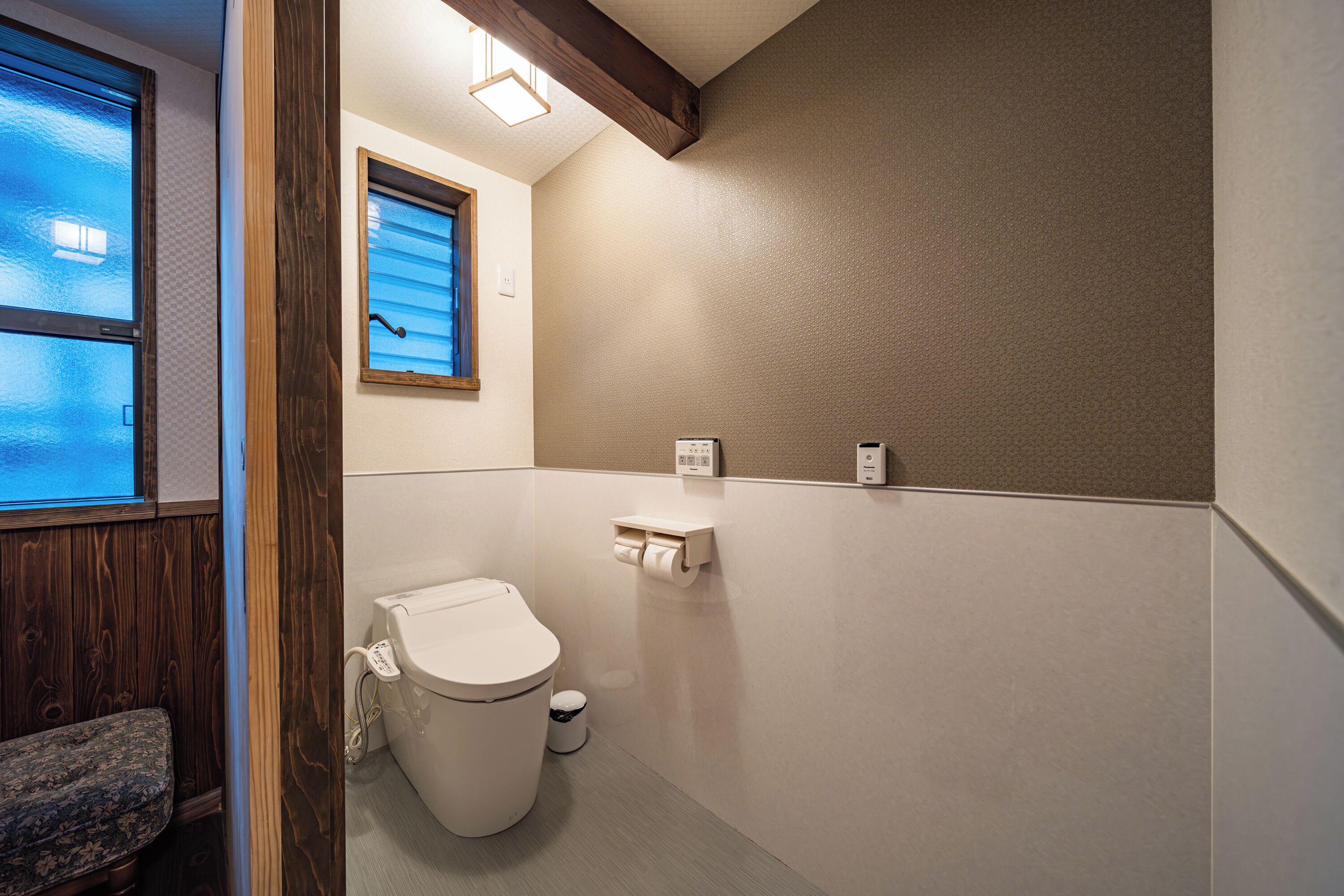 A small, modern bathroom with a toilet, a window, and a wooden bench.