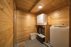 A compact, wooden-paneled room with a washing machine, a small laundry basket, and a cabinet.