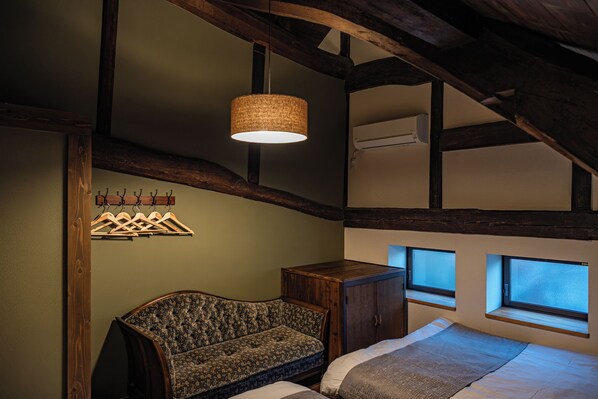 A room with a wooden ceiling, a hanging light fixture, a sofa, a cabinet, and two windows. - Aburaya Bettei (Beppu)