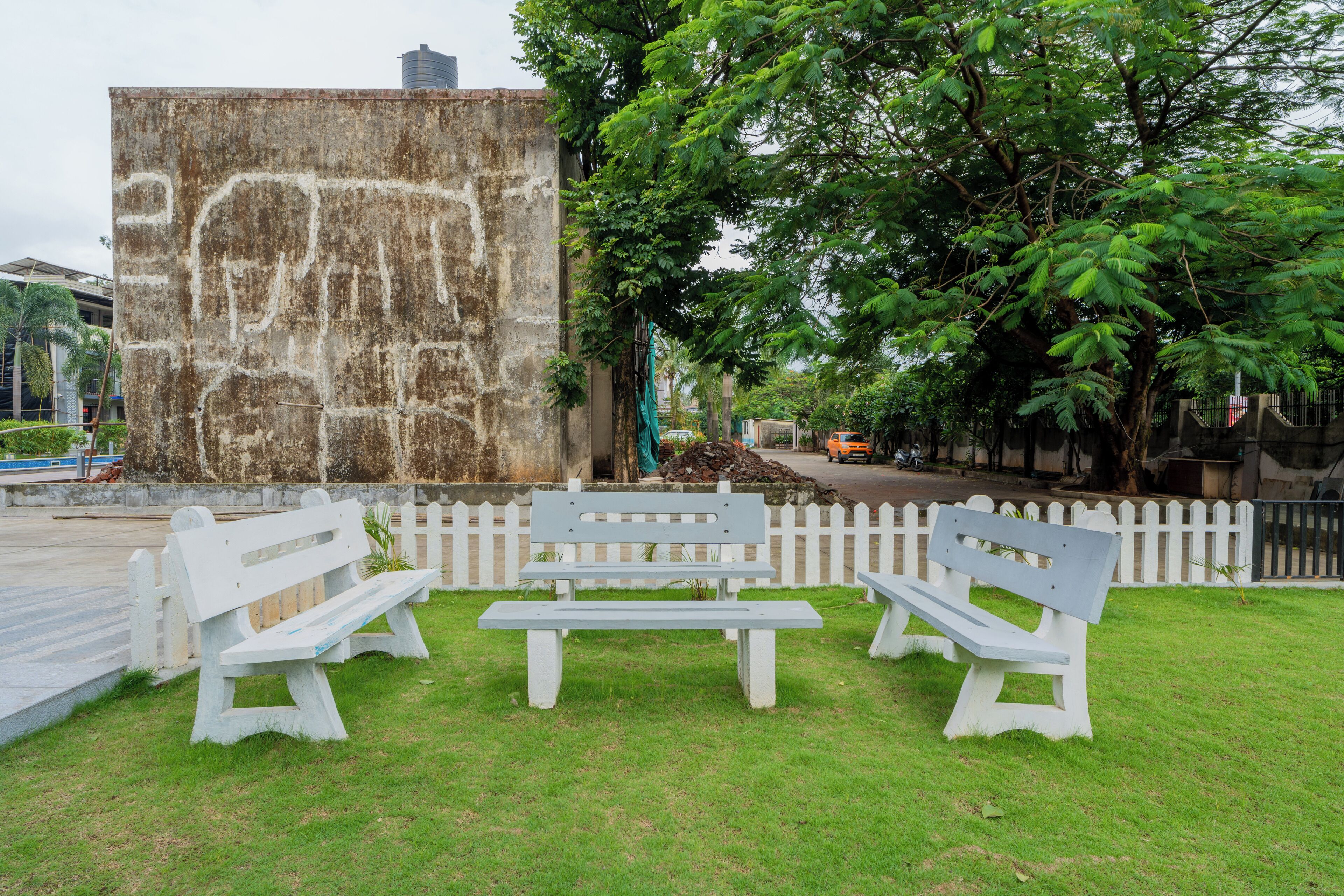 A park with three white benches and a white picket fence.