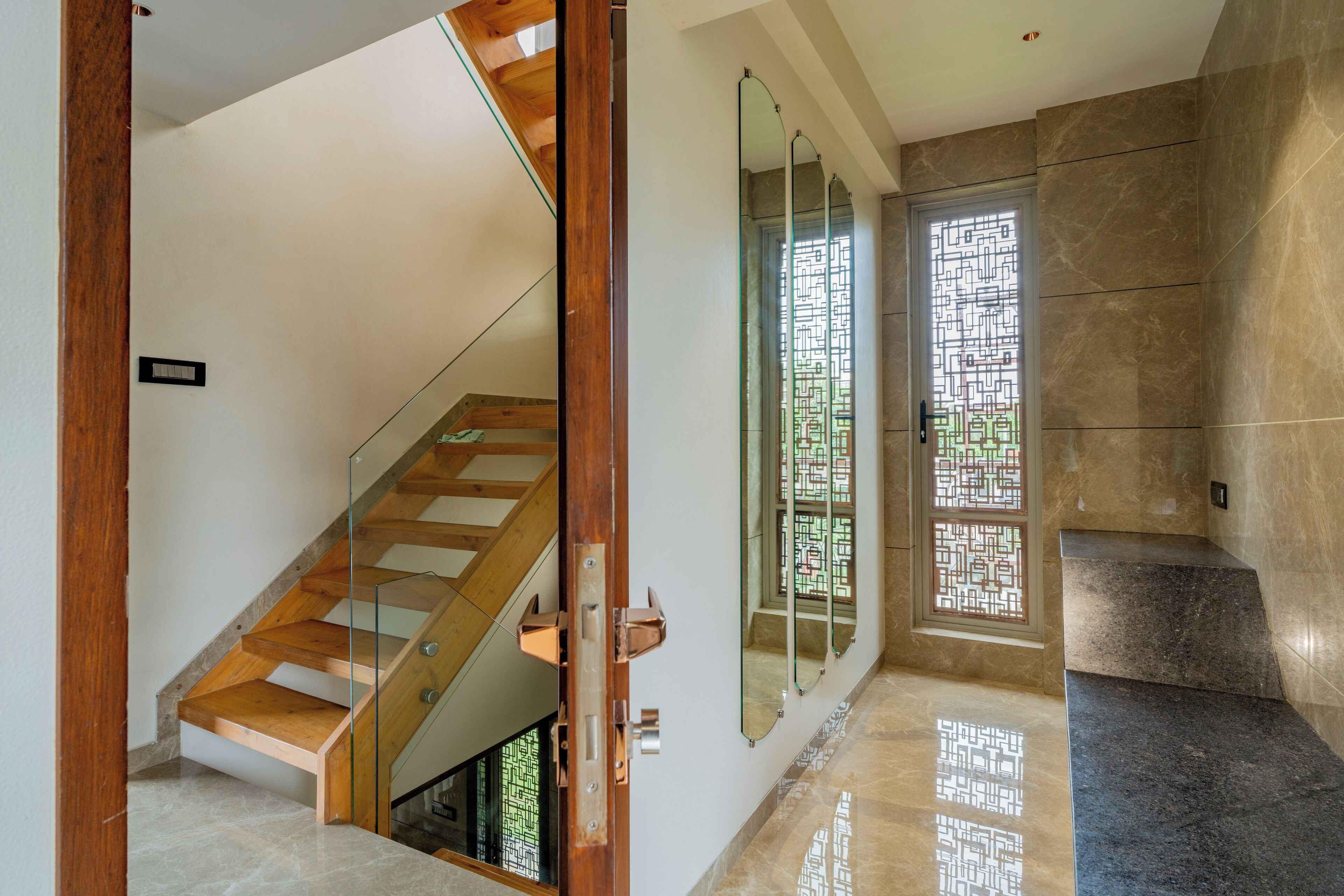 Un interior moderno con una escalera de madera, una puerta de cristal con diseño geométrico y suelo de baldosas.
