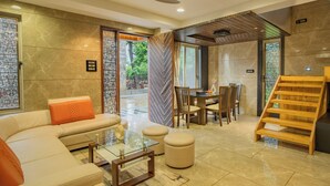 A modern living room with a sofa, ottomans, a glass coffee table, and a wooden staircase. - Alaya Stays 3-BHK with Pool near Khandala Hills - Imperial Serenia (Lonavala)