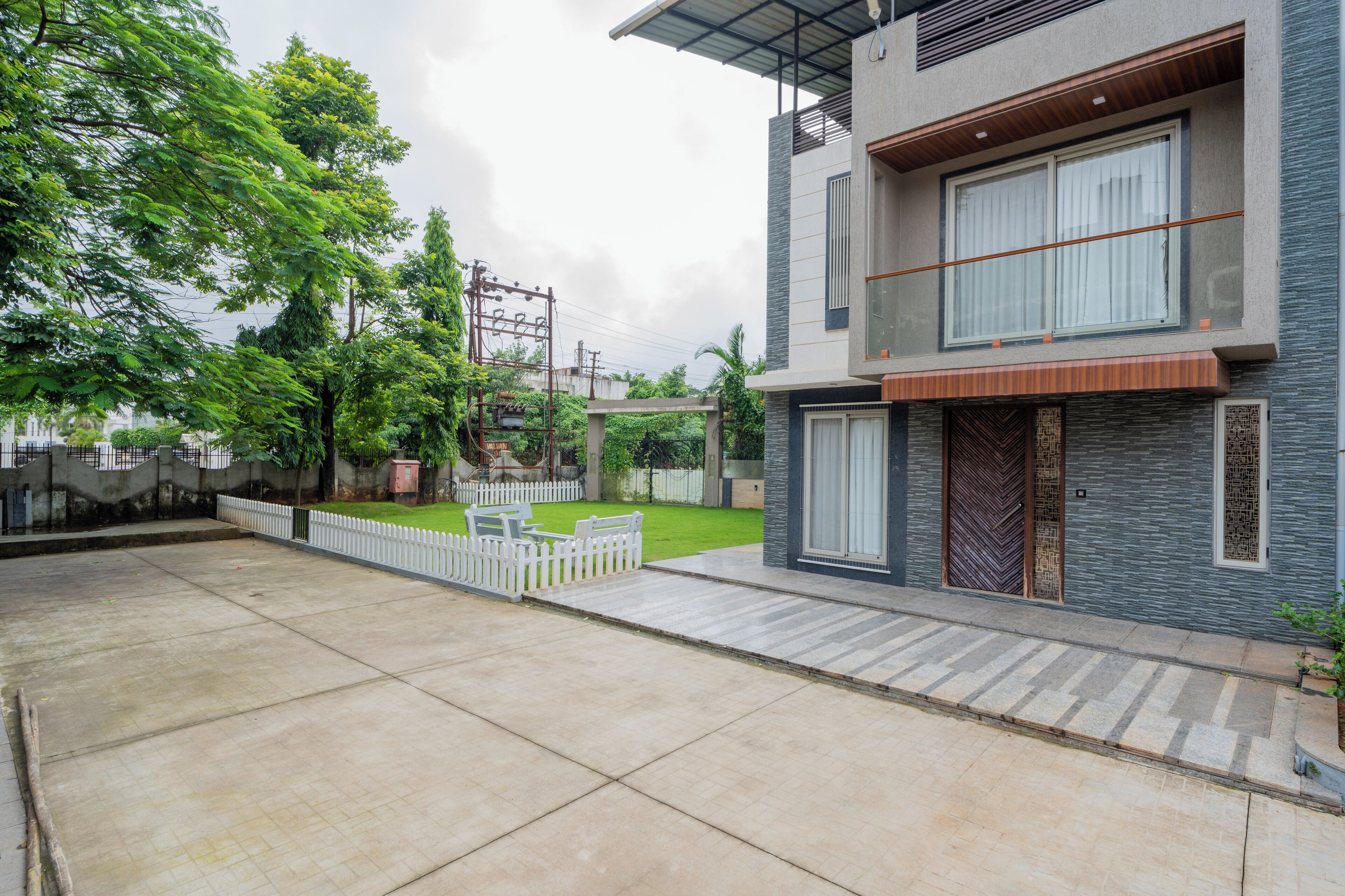 A modern two-story house with a spacious patio, a white picket fence, and a well-maintained lawn.