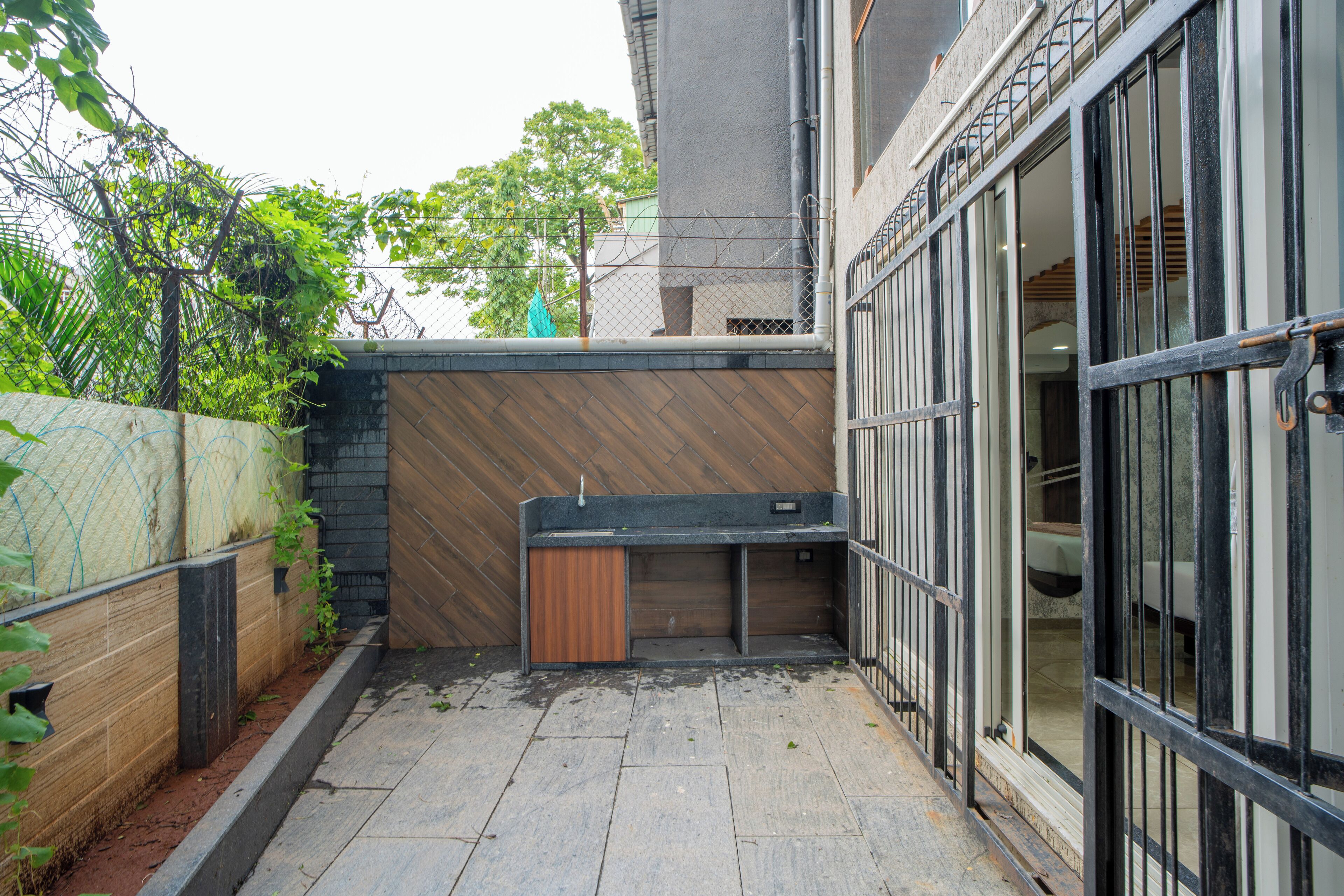 A narrow outdoor corridor with a wooden bench, a metal gate, and a concrete wall.
