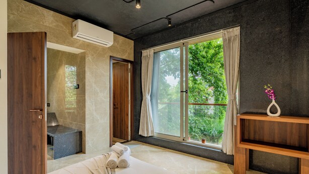 A modern bedroom with a large bed, a built-in shower, and a window with a view of greenery. - Alaya Stays 3-BHK with Pool near Khandala Hills - Imperial Serenia (Lonavala)