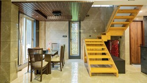 A modern interior with a wooden staircase, a dining area with chairs and a table, and a decorative wall panel. - Alaya Stays 3-BHK with Pool near Khandala Hills - Imperial Serenia (Lonavala)