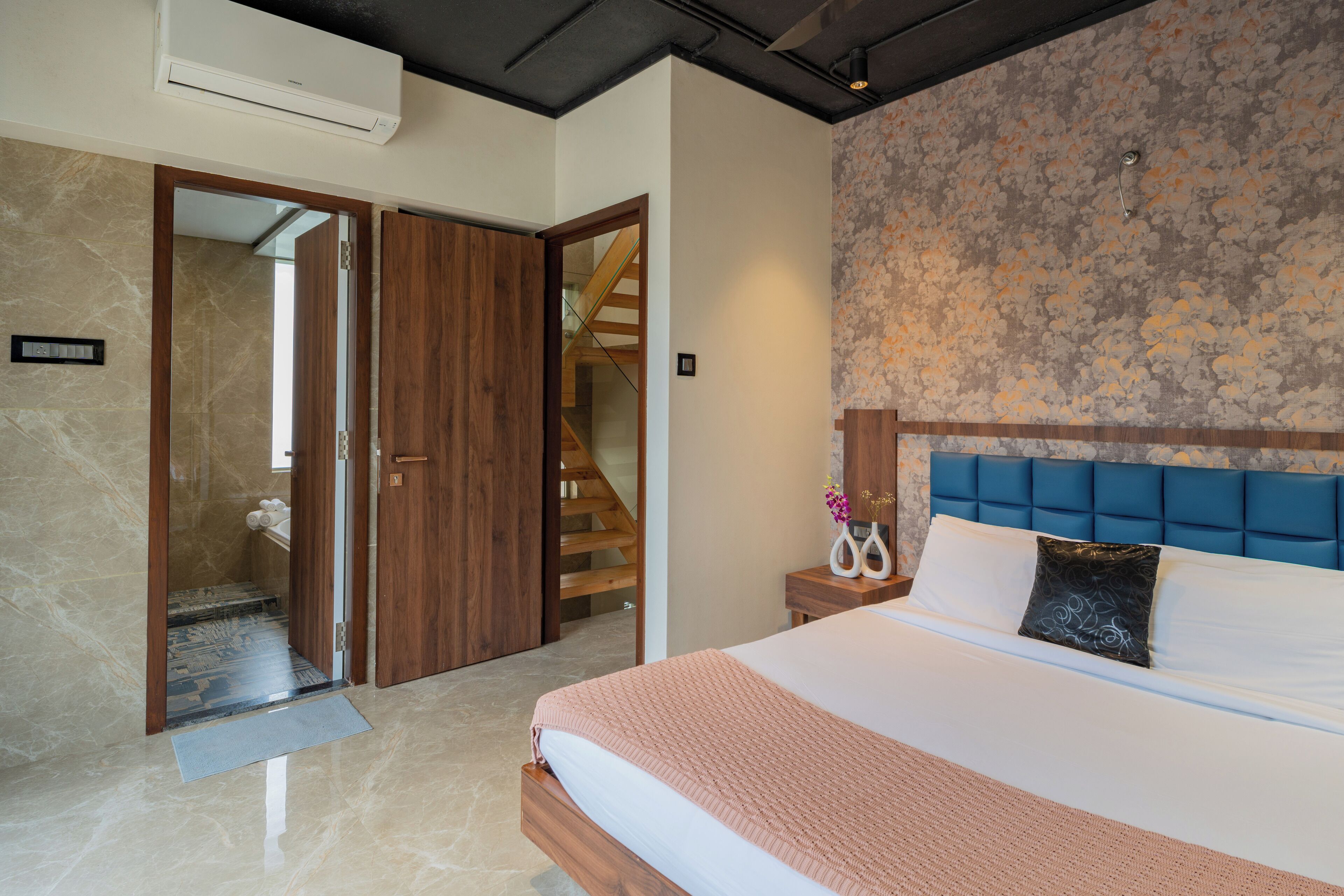 A bedroom with a large bed, wooden door, and a staircase leading to a bathroom.
