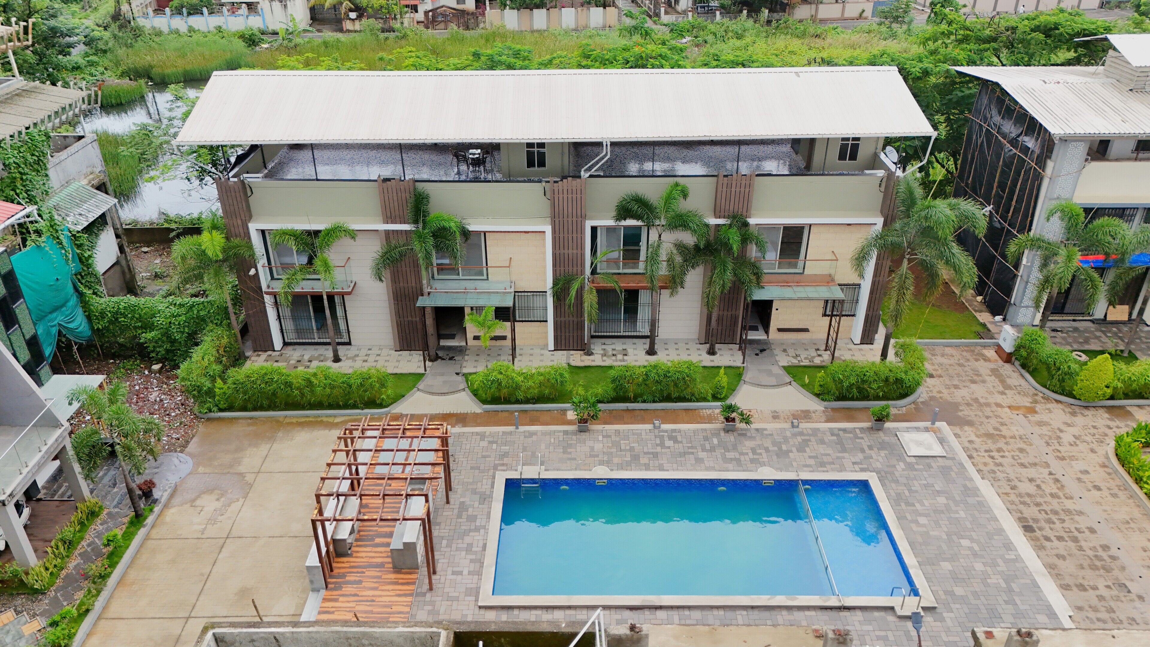 A modern residential building with a swimming pool, surrounded by greenery and a small garden area.