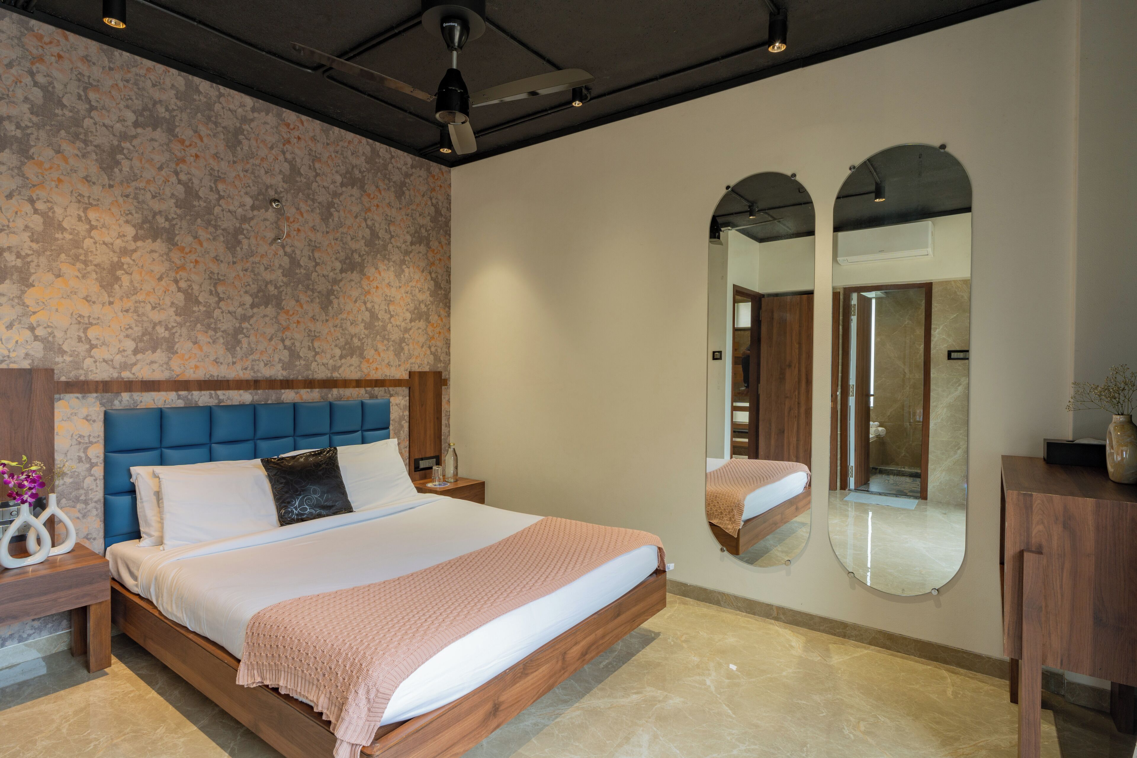 A modern bedroom with a large bed, a wooden headboard, a nightstand, a mirror, and a wooden dresser.