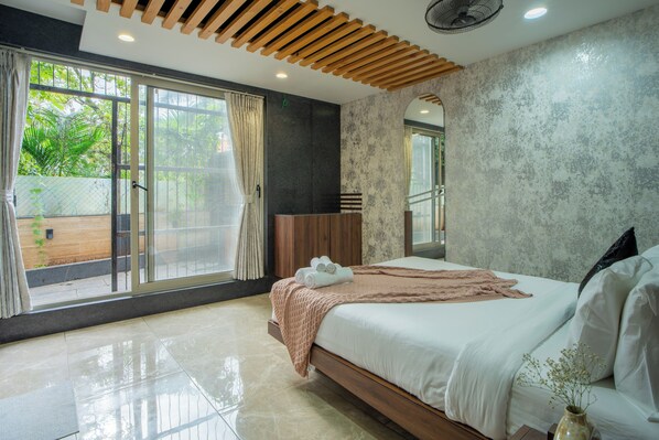 Un dormitorio moderno con una cama grande, puertas de cristal correderas a un balcón y vistas a zonas verdes.