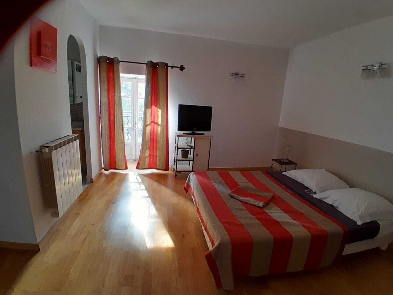 A bedroom with a bed, a TV, a radiator, and a window with curtains.