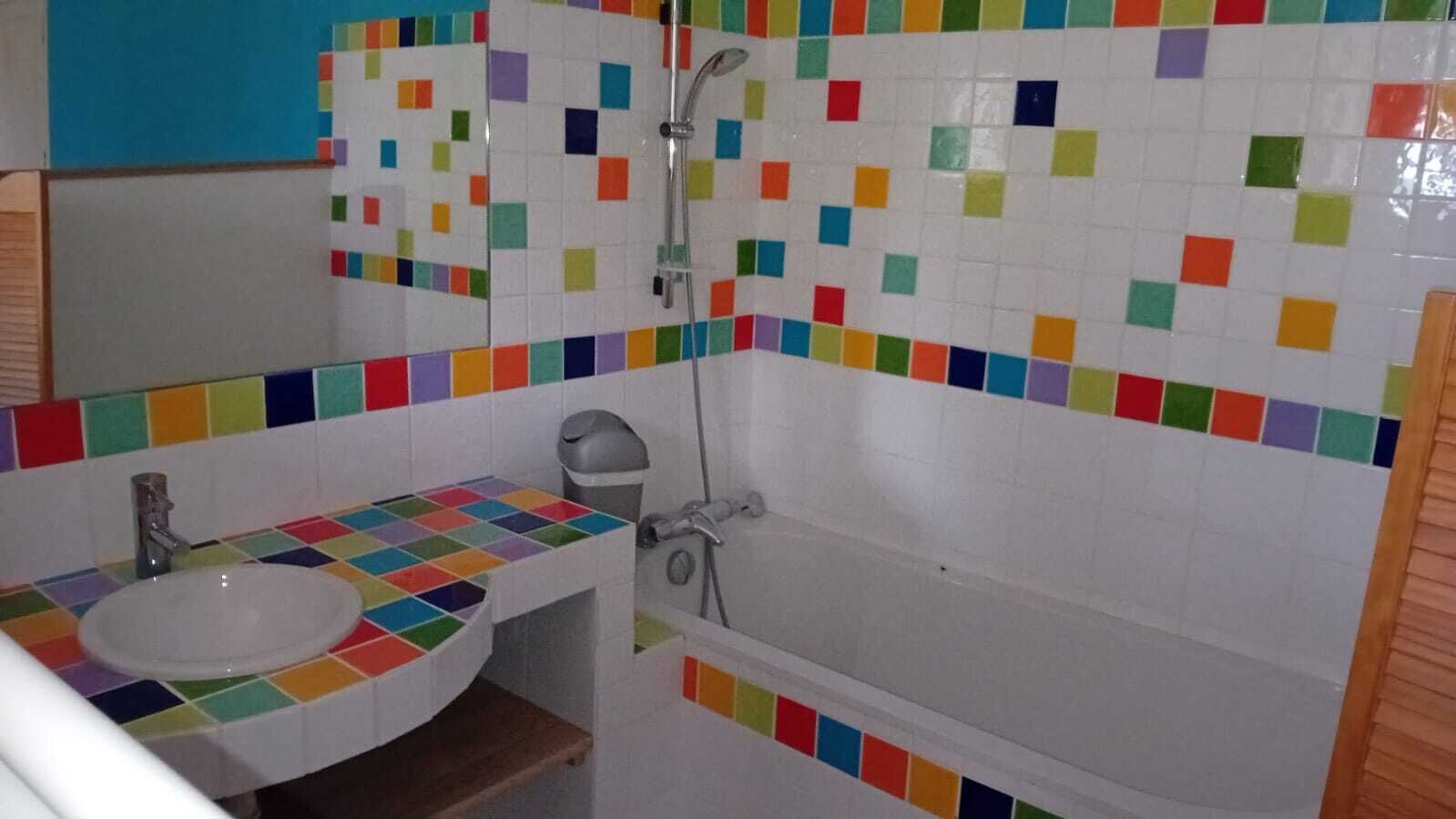 Une salle de bain avec un mur recouvert de mosaïques colorées, un lavabo blanc et une baignoire.