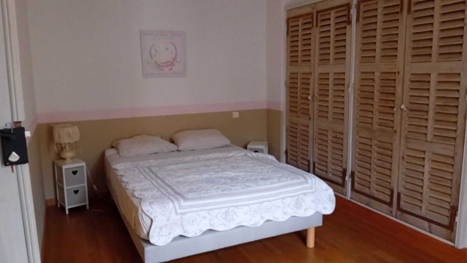 Um quarto com cama, mesas de cabeceira, abajur e guarda-roupa.