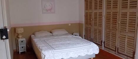 Um quarto com cama, mesas de cabeceira, abajur e guarda-roupa.