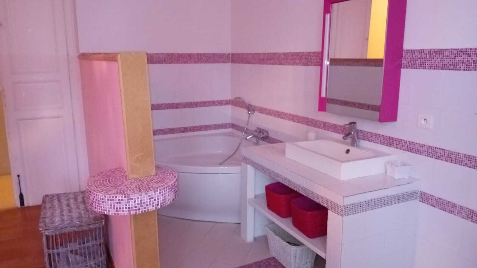 A bathroom with a white bathtub, a white sink, and a mirror above the sink. There are red storage bins under the sink and a small wicker basket on the floor.