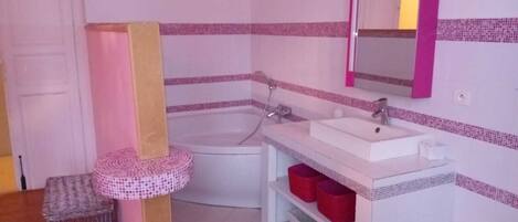 A bathroom with a white bathtub, a white sink, and a mirror above the sink. There are red storage bins under the sink and a small wicker basket on the floor.