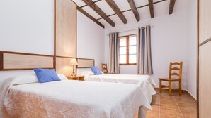 A hotel room with two beds, a wooden chair, a nightstand, and a window with curtains.