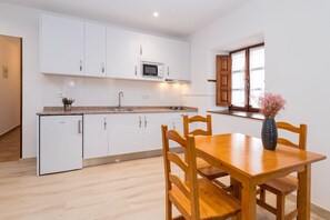 Une cuisine moderne avec des meubles blancs, un four à micro-ondes et un évier. On y trouve une table à manger en bois, des chaises et un vase avec des fleurs.