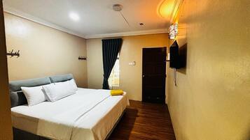 A bedroom with a bed, a wall-mounted TV, a door, and a window with curtains.