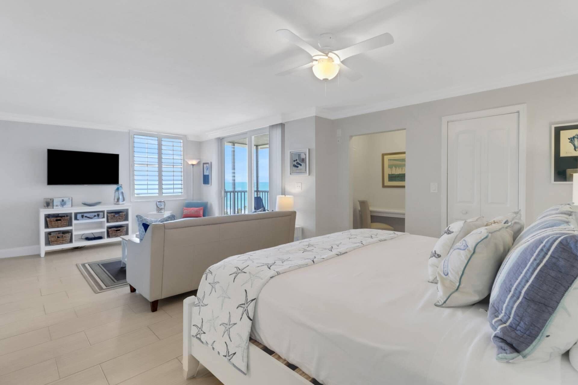 A bedroom with a bed, a TV, a sofa, and a balcony with a view.