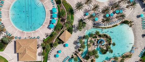 An aerial view of a resort with multiple swimming pools, sun loungers, and palm trees.