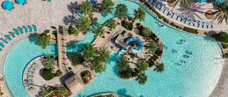 An aerial view of a resort with a winding pool, sun loungers, and palm trees.
