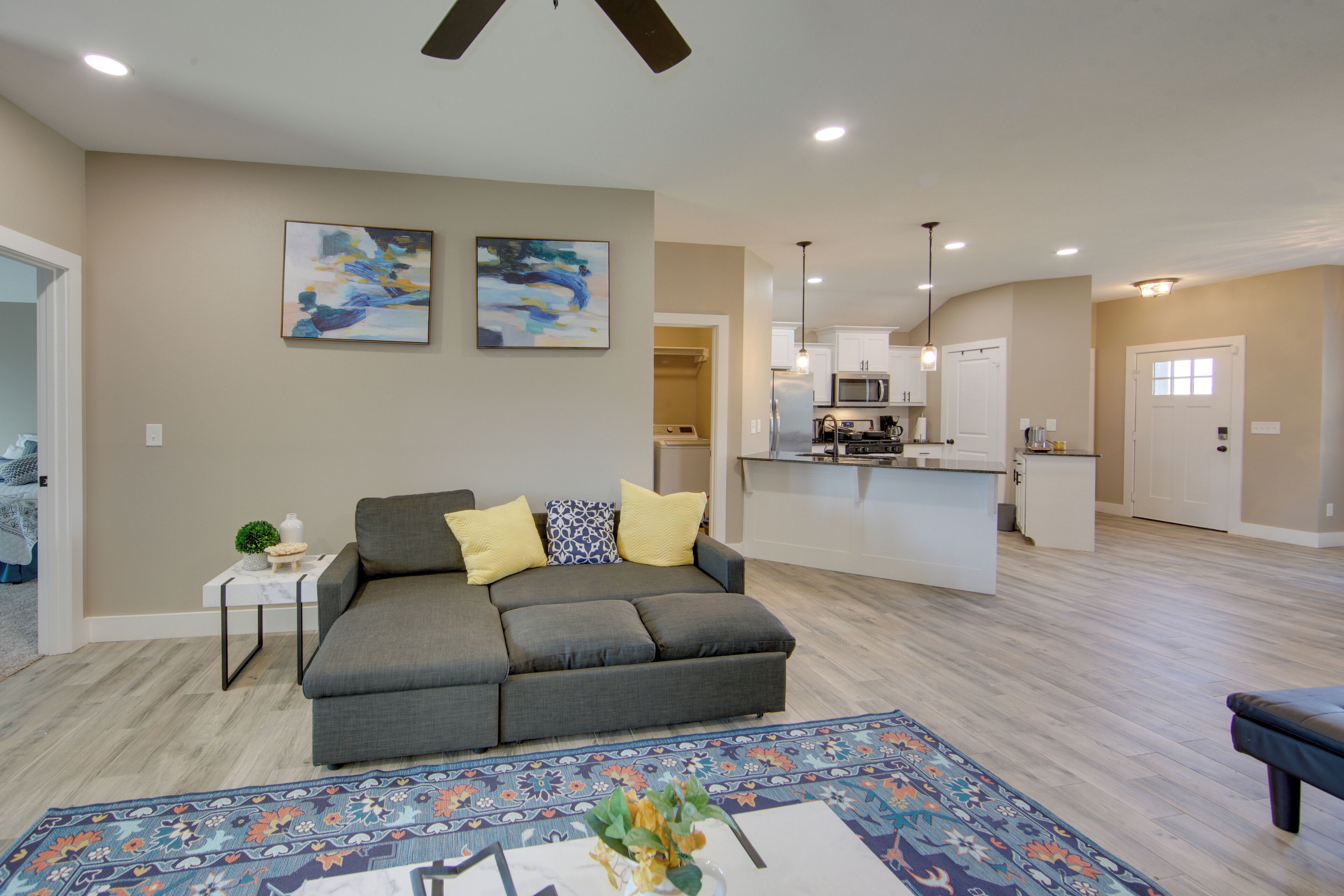 A spacious living room with a grey sectional sofa, a patterned rug, and abstract wall art.