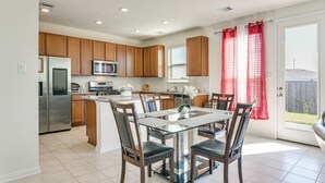 A modern kitchen with wooden cabinets, a stainless steel refrigerator, and a glass dining table with chairs. - 11 Mi to Beach: La Marque Home w/ Patio! (La Marque)