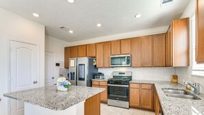 A modern kitchen with granite countertops, wooden cabinets, stainless steel appliances, and a central island. - 11 Mi to Beach: La Marque Home w/ Patio! (La Marque)