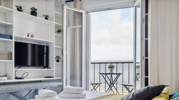 A hotel room with a bed, a TV, a balcony with a table and chairs, and a view of the water.