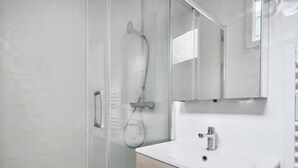 A modern bathroom with a glass shower enclosure, a white sink, and a wooden vanity.