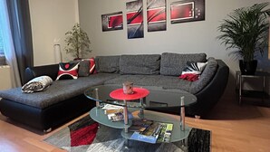 A modern living room with a sectional sofa, a glass coffee table, and abstract wall art. - Spacious, bright apartment with balcony, quiet location with good transport links (Bad Berneck im Fichtelgebirge)