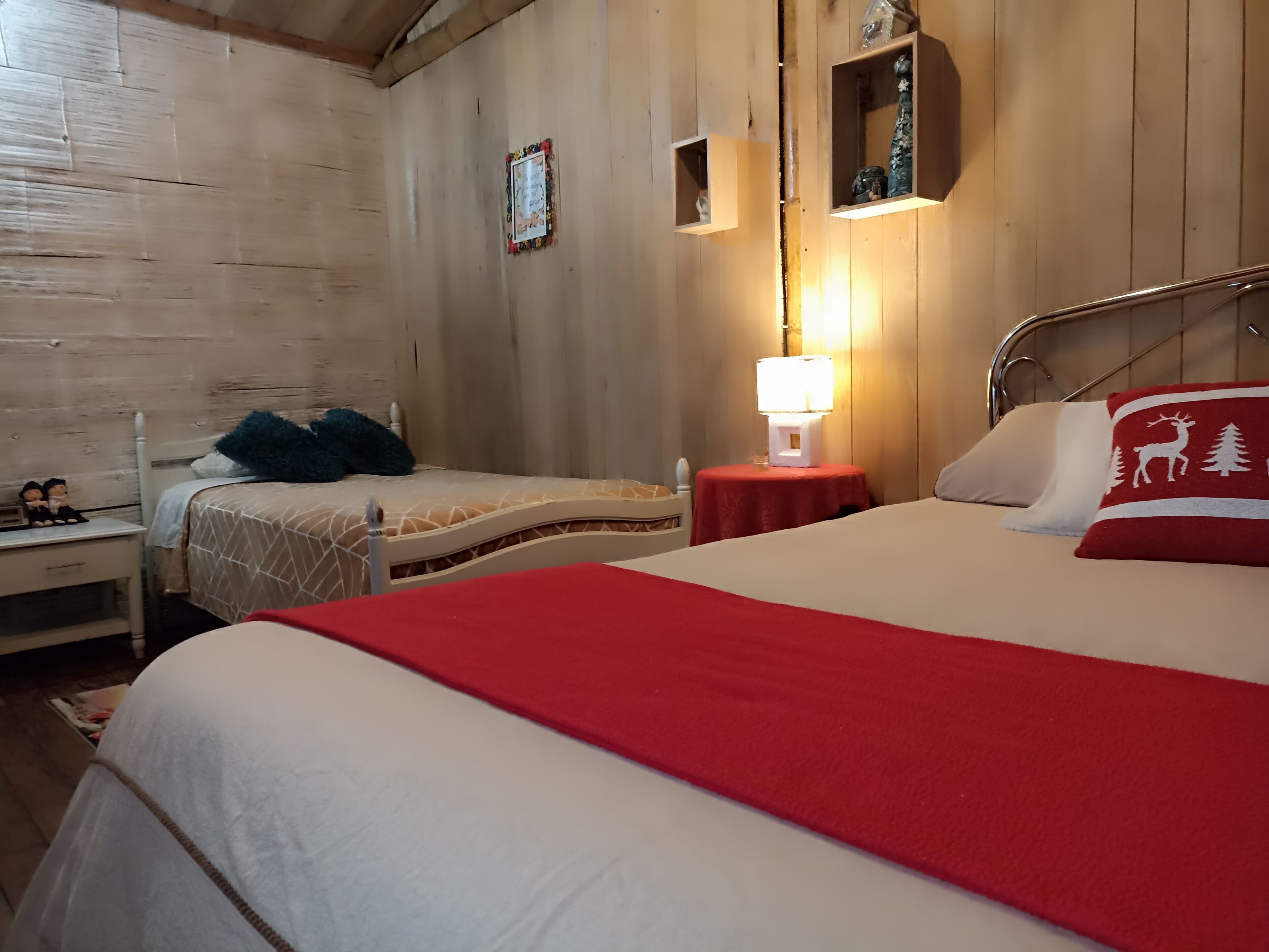 Ein Zimmer mit zwei Betten, einem Nachttisch, einer Lampe und einer Holzwand.