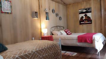 Una habitación con dos camas, paredes de madera, una mesita con una lámpara y objetos decorativos.