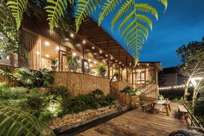 A wooden building with a covered outdoor area, surrounded by lush greenery and a stone wall. - De Ma'at villa (Xuan Huong - Da Lat)