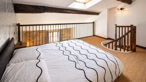 A bedroom with a bed, a skylight, a wooden staircase, and a stone wall.