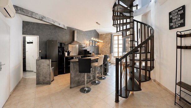 A modern kitchen with a central island, a spiral staircase, and a stone accent wall.