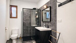 A modern bathroom with a glass shower enclosure, a white toilet, and a black vanity with a mirror.