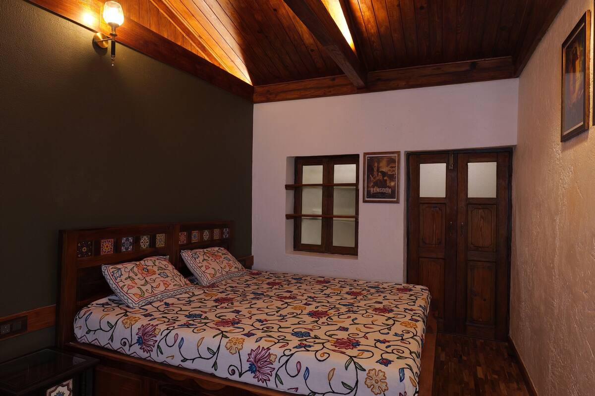 A bedroom with a wooden ceiling, a bed with floral bedding, a nightstand, and a wall-mounted light fixture.