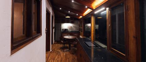 Un couloir étroit, doté d’un plancher et de murs en bois, mène à un espace cuisine comprenant une table à manger et des chaises.