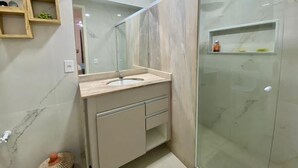 A modern bathroom with a marble sink, a glass shower enclosure, and built-in shelves. - Pousada alto das arvores (Buzios)